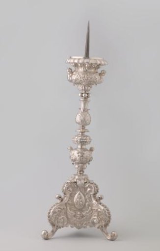 Silver candelabrum with five-sectioned baluster stem on triangular base with scroll feet. Decorated with medallions containing Christ, Peter, and Ignatius