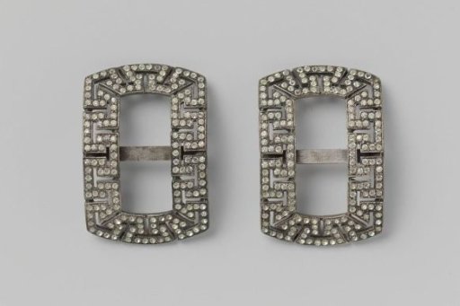 Shoe buckle of silvered metal in the shape of a horizontal rectangle, within which angular meanders, set with paste