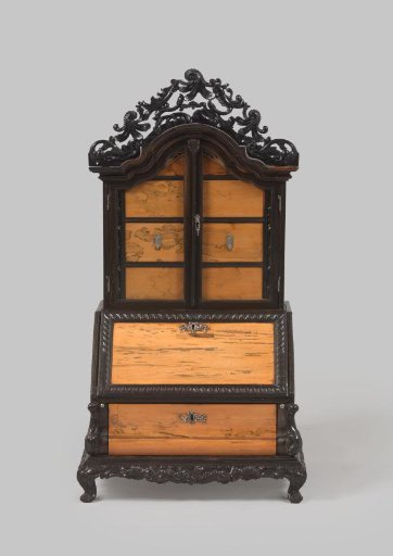 Bureau on a separate pedestal with obliquely placed curved legs, decorated with floral and leaf work, volutes and rocailles. Double-curved lower cabinet with drawer. Top with sloping flap with knorren edge. Upright with two doors with glass panes concealing drawers. Silver fittings.
