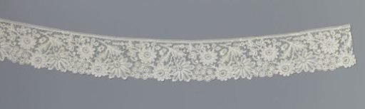 Strip of bobbin lace with two daisies and a cluster flower next to a hanging flower with nine lobes