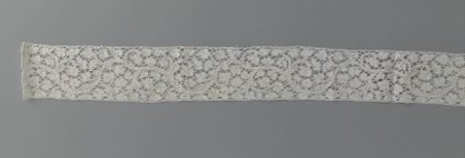 Strip of bobbin lace with a running pattern of volute scrolls with flowers and buds