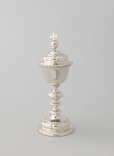 Ciborium of silver with smooth foot, stem and cover. On the cover a globe with cross. Cup inside gilded