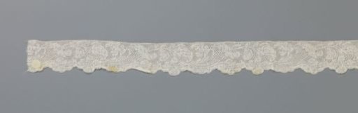 Strip of bobbin lace with a cornucopia closed by an acanthus leaf