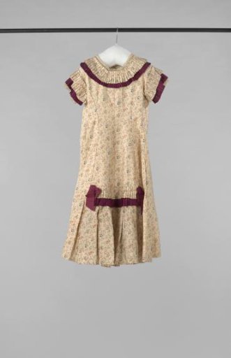 A party dress of printed cream silk with flower sprigs, trimmed with carmine red ribbons and strips