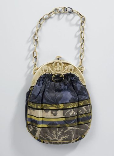 Reticule with rounded handle of ivory-coloured celluloid, with a Buddha in relief between two elephants, and a pouch of blue, green, black and beige floral and striped satin, chain of ivory-coloured celluloid