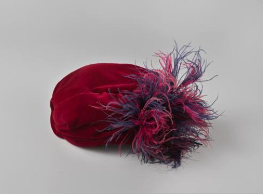 Hat in toque model of dark red velvet, on the left side decorated with a small tuft of ostrich feathers in dark red and blue