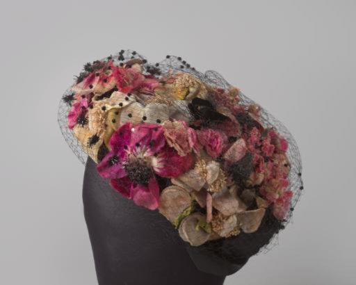 Hat with black bow in pillbox style of black straw, entirely covered with multicoloured flowers under a hanging black voile with studs and rhinestones