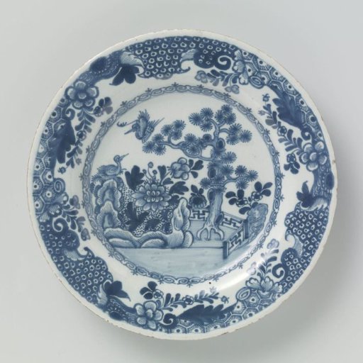 Plate, painted flat on the ground with a fence, tree, rocks, flowers and two birds