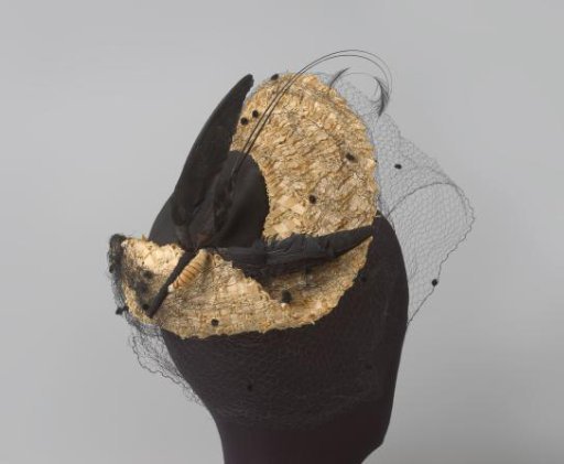 Hat with a flat pancake-shaped dome, with puffed voile and on the right a plume like a flying bird of feathers
