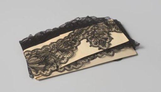 Strip of double-sided scalloped black machine-made lace with flower motif with contour threads, on cardboard