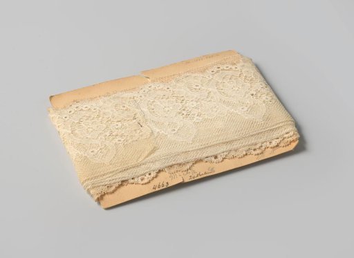 Strip of white lace with one straight side, the other side scalloped and picoted, on cardboard
