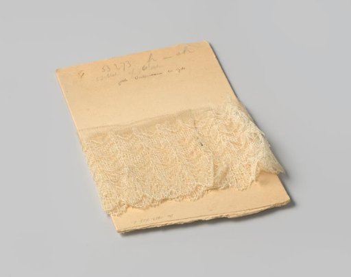 Strip of white lace with a meander motif on cardboard