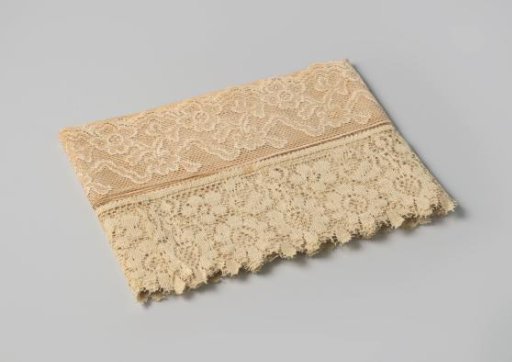 Strip of white lace, scalloped on one side decorated with a floral motif, on cardboard