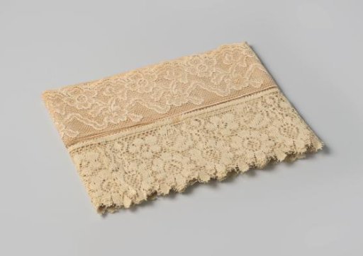 Strip of white lace, scalloped on one side, decorated with a floral motif, on cardboard