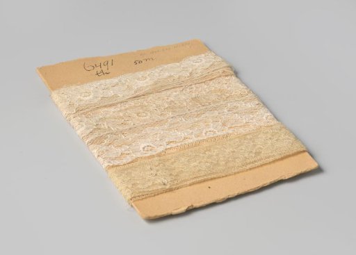 Strip of white machine-made lace with a pattern of flowers, scalloped on one side and provided with picots, on cardboard