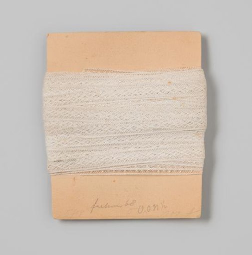 Insert of white lace, decorated with strung ovals between rosettes on cardboard