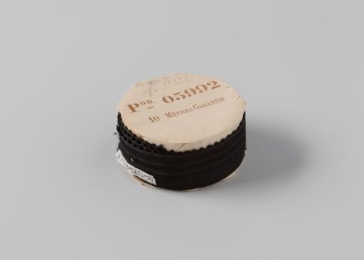 Ribbon on a roll, black satin with two black stripes woven in the center, one side is scalloped and trimmed with a wavy border in black
