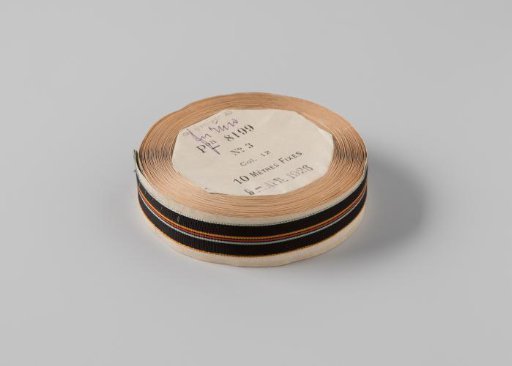 Ribbon on a roll, striped, the ribbon is black with three woven stripes in the center in the colors orange, red and light blue, and is edged on the sides with light blue and orange embroidery respectively
