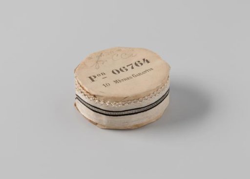 Ribbon on a roll, white satin with a central stripe of openwork flanked by two black stripes, one side scalloped and edged with a wavy white border