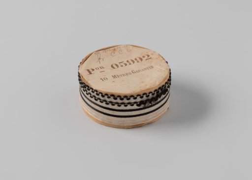 Ribbon on a roll, white satin with two black stripes in the middle, one side scalloped and edged with a wavy black border