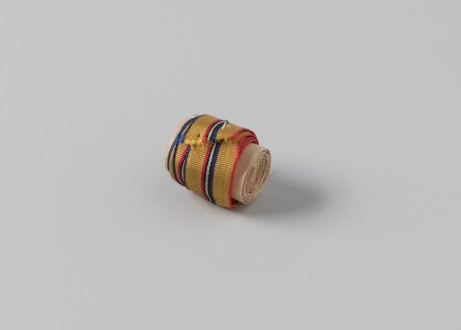 Ribbon, striped, the ribbon is yellow with three woven stripes in the middle in the colors red, blue, light green and black and is edged on the sides with respectively light blue and orange embroidery