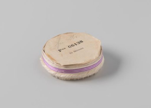 Roll of white ribbon with one frayed side and three purple horizontal stripes, and a loose piece of the same ribbon