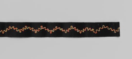 Roll of black satin ribbon with multicoloured embroidered wavy motif on cardboard