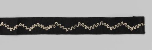 Roll of black satin ribbon with white embroidered wavy motif on cardboard