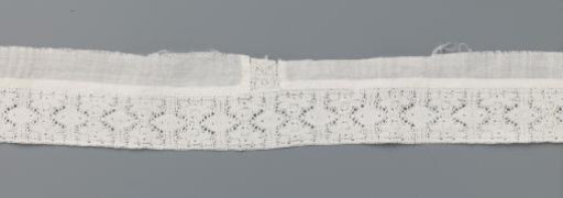 Strip of bobbin lace with two stylised mirrored flowers between vertical lines and ovals