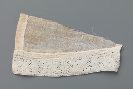 Small strip of bobbin lace with stylised flower between two vertical lines and ovals on a triangular fragment of linen batiste
