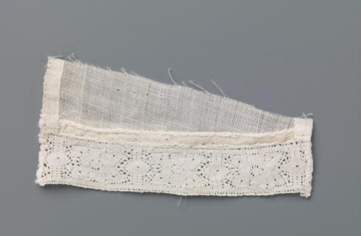 Strip of bobbin lace with stylized flower between two vertical lines and ovals on a triangular fragment of linen batiste