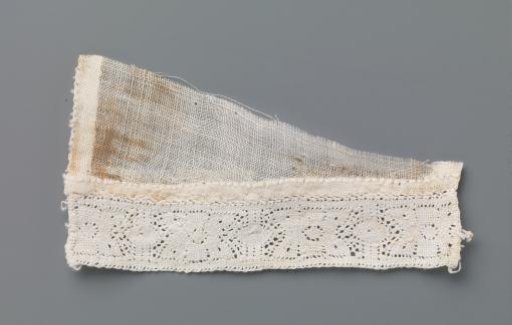 Strip of bobbin lace with stylized flower between two vertical lines and ovals on a triangular fragment of linen batiste