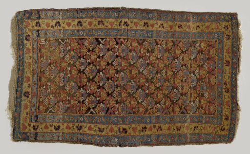 Flower carpet with diagonally placed flowers in blue and mustard yellow on a brown ground. Triple border with pink and white flowers, zigzag leaves, and brown vines.
