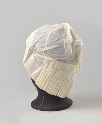 Cap of linen batiste, the unadorned crown trimmed with a strip of linen batiste pleated along the forehead