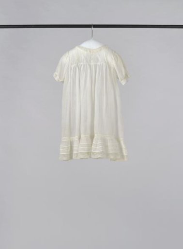 Child's dress with short puffed sleeves and back fastening with three mother-of-pearl buttons of white glass batiste, decorated with horizontal and vertical smocking and Valenciennes lace