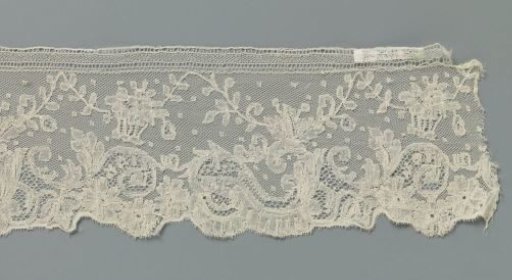 Strip of bobbin lace with zigzag scroll above a border with S-scrolls