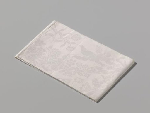 Napkin of white linen damask with a pattern of putti with decorative tassels and monograms in the corners