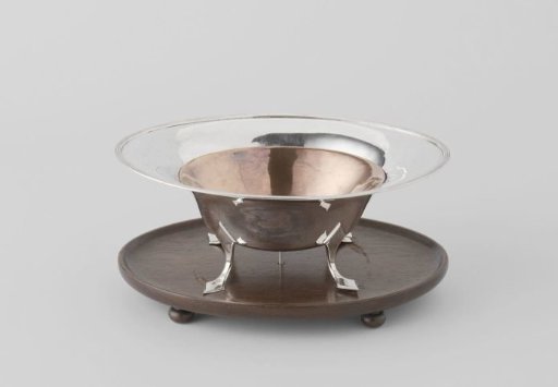 Pipe warmer of silver with four curved legs on a mahogany top. Inner bowl of red copper. Top on four ball feet.