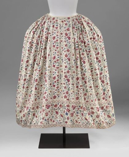 Skirt of white cotton with vertical stripes and a wide lower border of tamboured multicoloured floral and leaf vines, separated by stripes or stylised ornamental borders
