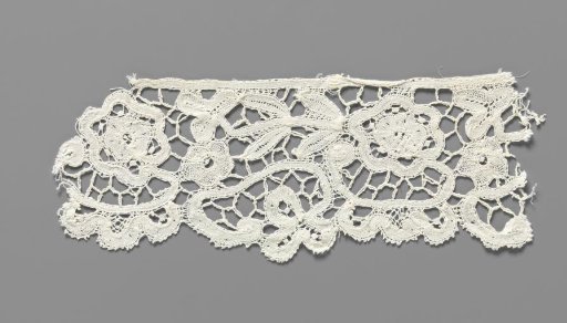 Cuff of a strip of bobbin lace with a rosette flower on a C-shaped stem with three lobes hanging below