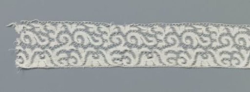 Strip of machine-made lace with hanging cup-shaped flower between loose S-scrolls
