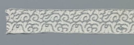 Strip of machine-made lace with hanging cup flower between loose S-scrolls