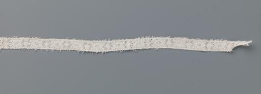 Small strip of bobbin lace with stylized flower between two vertical lines and ovals on a rectangular fragment of batiste