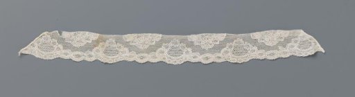 Border strip of bobbin lace with cartouches along the lower edge alternating with halved flowers along the upper edge