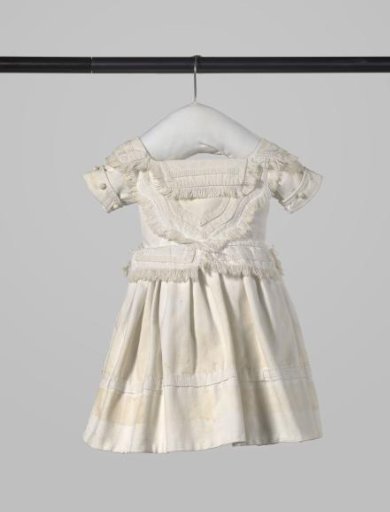 Child's dress with short sleeve with turned-down edge and round buttons and loose flaps along the waist and neck of white piqué, decorated with passementerie and fringes