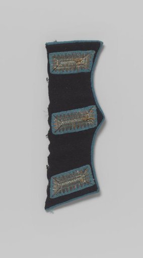 Pocket flap of dark blue cloth with three blind buttonholes around which is embroidered with silver thread