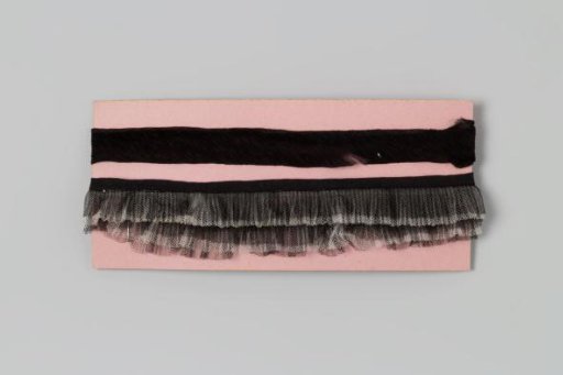 Two black ruffles wound around a piece of rose-colored cardboard
