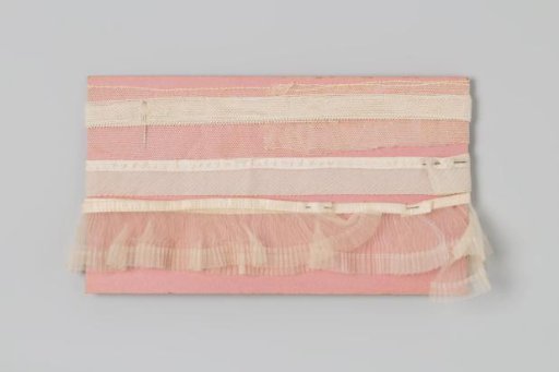 Three white ruffles wound around a piece of rose-colored cardboard