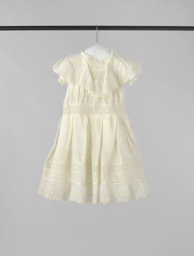 A girl's dress of batiste and strips of English embroidery, with pelerine collar and pleated skirt