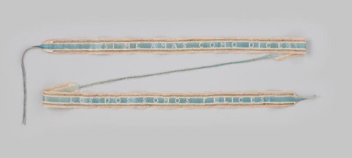 Garter of white linen woven with blue and red silk and metal thread, with the inscription in the middle SI ME AMAS COMO DICES - LOS DOS SOMOS FELICES